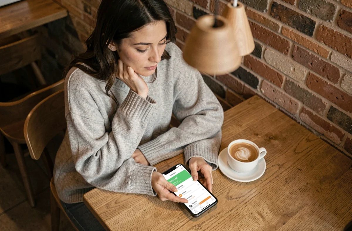 Femme consultant les prix de smartphones dans un café, comparaison Android et iOS